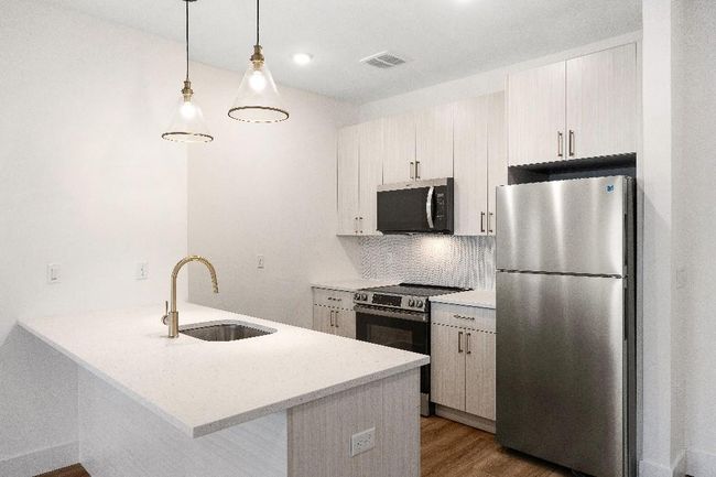 Kitchen featuring appliances with stainless steel finishes, a sink, wood finished floors, tasteful backsplash, and a peninsula | Image 9