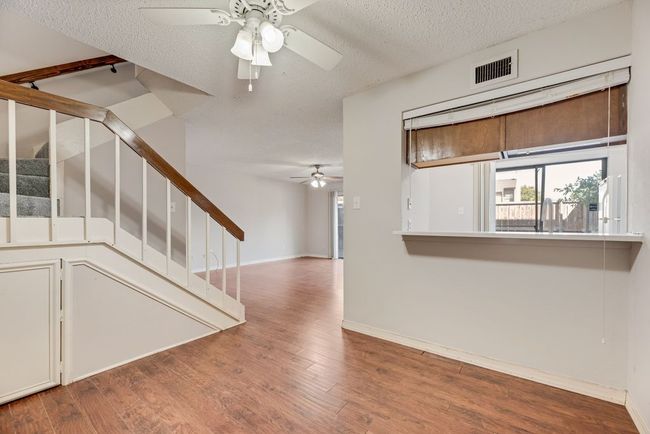 Unfurnished living room featuring ceiling fan, wood finished floors, a textured ceiling, and stairs | Image 7