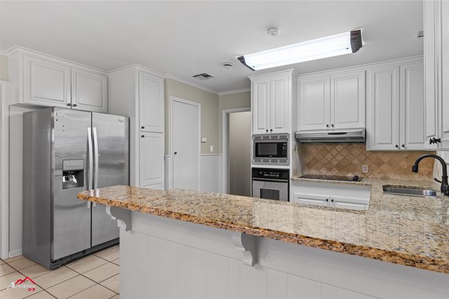 Kitchen featuring appliances with stainless steel finishes, a sink, white cabinets, light stone counters, and crown molding | Image 10
