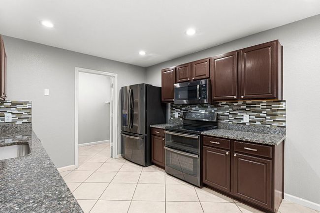 Kitchen featuring black appliances, decorative backsplash, dark brown cabinets, light tile patterned flooring, and dark stone countertops | Image 10