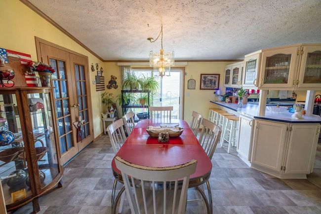 Dining space with a notable chandelier, stone finish flooring, crown molding, a textured ceiling, and french doors | Image 14