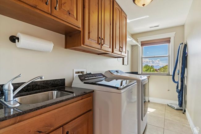 Washroom with visible vents, washing machine and clothes dryer, a sink, cabinet space, and light tile patterned floors | Image 46