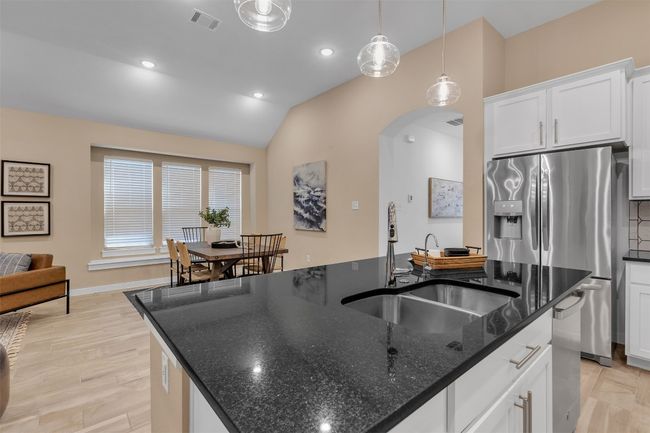 Kitchen featuring a kitchen island with sink, arched walkways, vaulted ceiling, stainless steel fridge with ice dispenser, and white cabinetry | Image 12