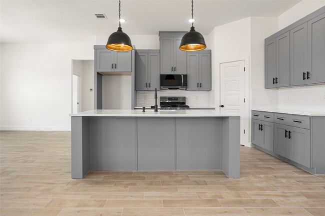 Kitchen with stainless steel appliances, gray cabinetry, tasteful backsplash, and an island with sink | Image 6