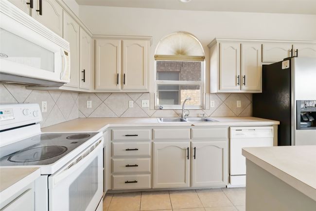 Kitchen with a sink, white appliances, light countertops, and light tile patterned floors | Image 8