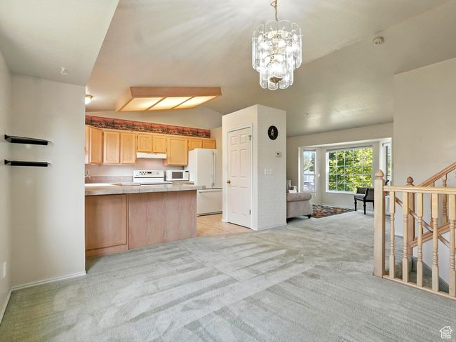 Kitchen featuring white appliances, light brown cabinets, light carpet, under cabinet range hood, and vaulted ceiling | Image 8