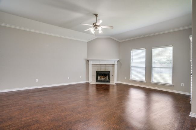 Unfurnished living room featuring ceiling fan, vaulted ceiling, a tiled fireplace, crown molding, and dark wood-type flooring | Image 5