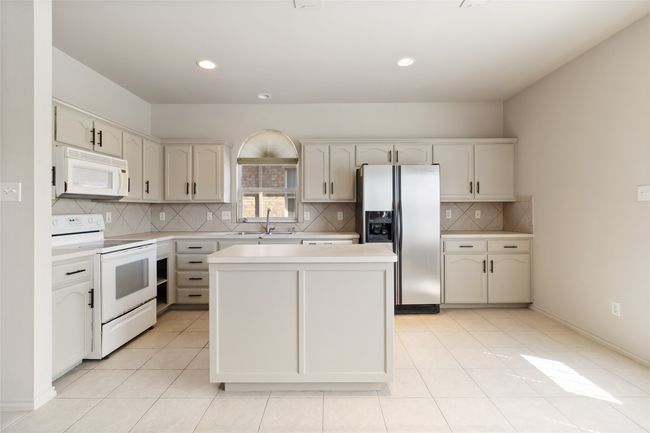 Kitchen featuring a center island, light countertops, light tile patterned flooring, white appliances, and a sink | Image 23