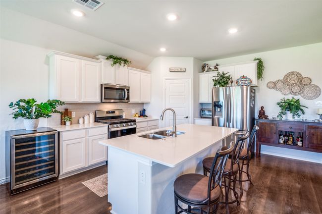 Kitchen featuring stainless steel appliances, beverage cooler, dark wood finished floors, decorative backsplash, and a kitchen bar | Image 12