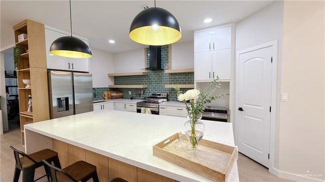 Kitchen with appliances with stainless steel finishes, open shelves, decorative backsplash, white cabinetry, and a breakfast bar | Image 4