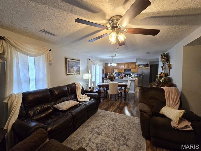 Living area featuring dark wood-type flooring, a ceiling fan, a textured ceiling, and plenty of natural light | Image 5