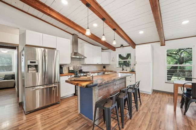 Kitchen featuring stainless steel refrigerator with ice dispenser, wall chimney range hood, a kitchen breakfast bar, backsplash, and a sink | Image 12