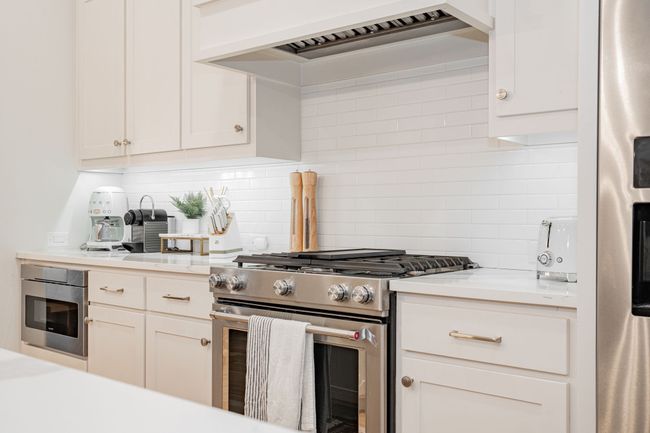 Kitchen with white cabinets, light countertops, stainless steel appliances, custom range hood, and backsplash | Image 10