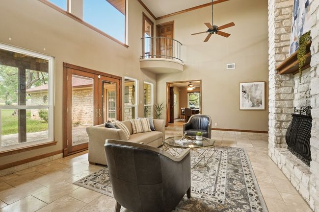 Living room with a ceiling fan, a towering ceiling, a stone fireplace, and french doors | Image 4