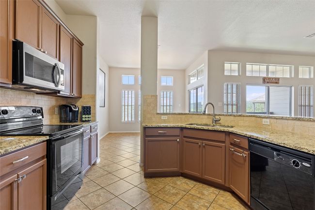 Kitchen with tasteful backsplash, light tile patterned floors, a sink, light stone counters, and black appliances | Image 27