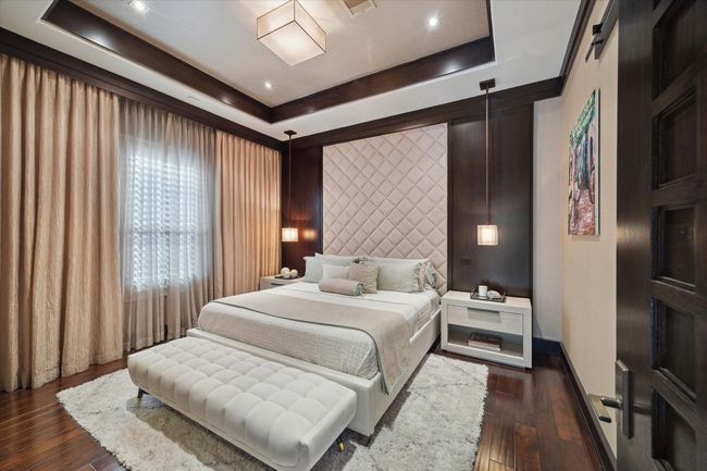 Tucked privately at the rear of the home, this secondary bedroom offers a serene guest retreat complete with a walk-in closet and adjoining bathroom. The tufted wall provides a stylish backdrop for the bed, flanked by deep wood walls and modern pendant lighting. The soft glow filtering through the Plantation shutters and upscale window treatments create a tranquil, retreat-like ambience. Thoughtfully appointed with sophisticated finishes, the suite evokes the elegance of a boutique hotel. | Image 31