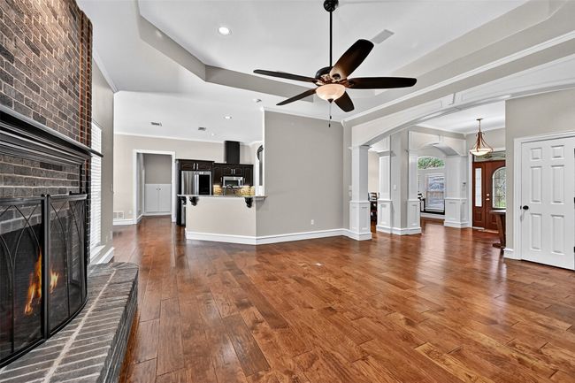 Unfurnished living room with arched walkways, a fireplace, ceiling fan, ornamental molding, and hardwood / wood-style flooring | Image 10