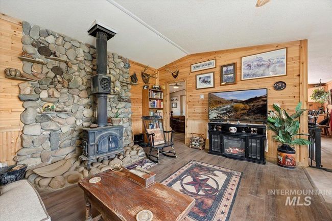 Living area featuring wood walls, lofted ceiling, a wood stove, wood finished floors, and a warm lit fireplace | Image 17