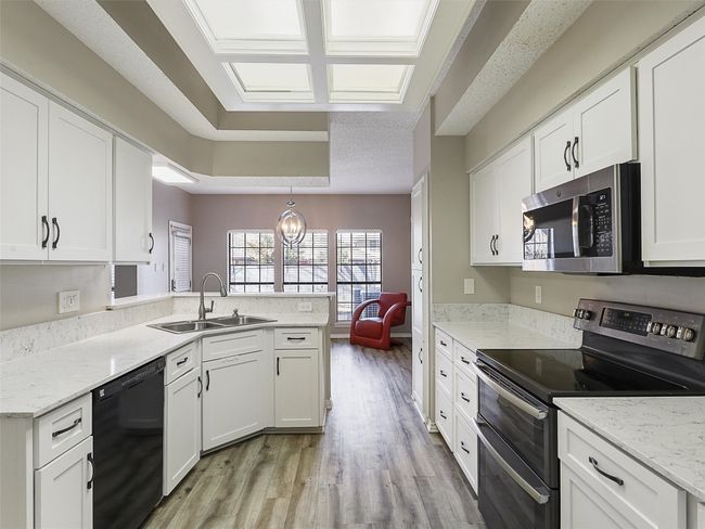 Kitchen with a peninsula, a sink, light wood-style floors, appliances with stainless steel finishes, and white cabinetry | Image 12
