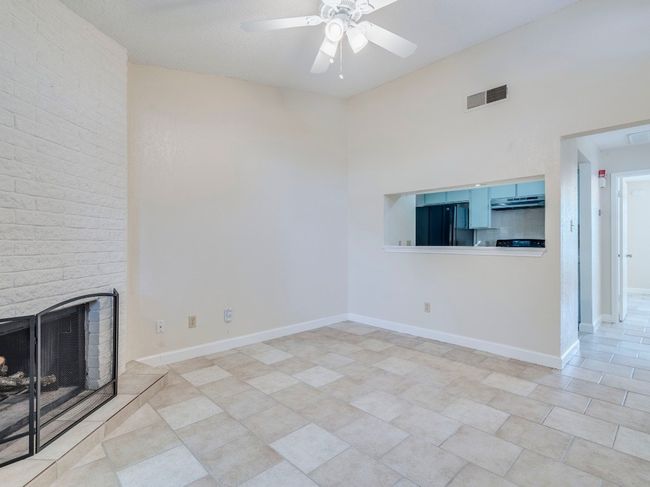 Unfurnished living room with ceiling fan, a brick fireplace, baseboards, and a high ceiling | Image 5