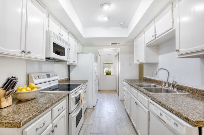 Kitchen with white appliances, a raised ceiling, and white cabinetry | Image 13