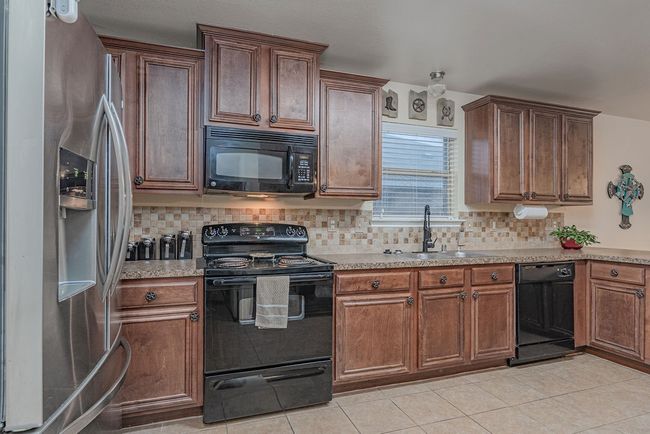 Kitchen with backsplash, light tile patterned floors, a sink, and black appliances | Image 12