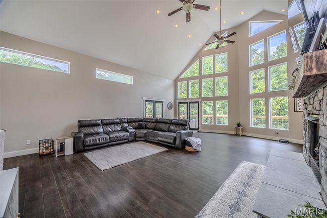 Living area featuring high vaulted ceiling, a stone fireplace, ceiling fan, wood finished floors, and recessed lighting | Image 6