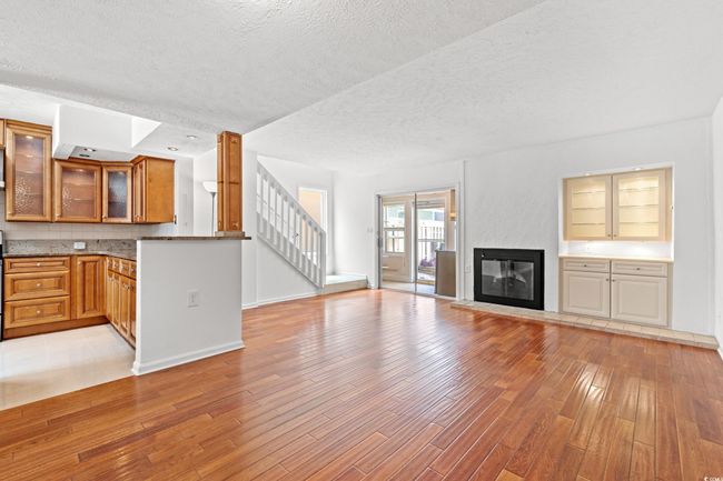 Unfurnished living room featuring light wood finished floors, a textured ceiling, stairway, and a glass covered fireplace | Image 5