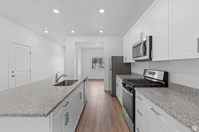Kitchen with white cabinets, a sink, recessed lighting, wood finished floors, and stainless steel appliances | Image 5