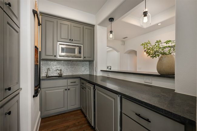 Kitchen featuring stainless steel microwave, gray cabinetry, dark countertops, a sink, and dark wood-style flooring | Image 19