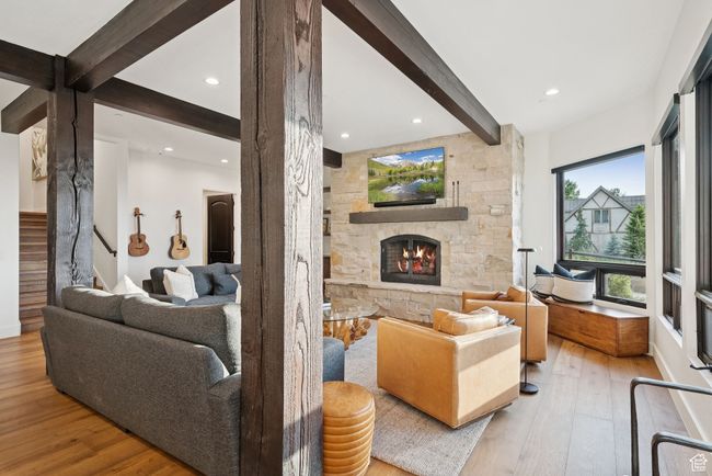 Living area featuring beamed ceiling, hardwood / wood-style floors, a stone fireplace, stairs, and recessed lighting | Image 48