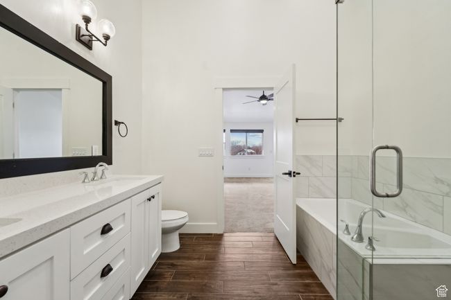 Bathroom featuring wood tiled floor, toilet, a tub to relax in, double vanity, and a sink | Image 28