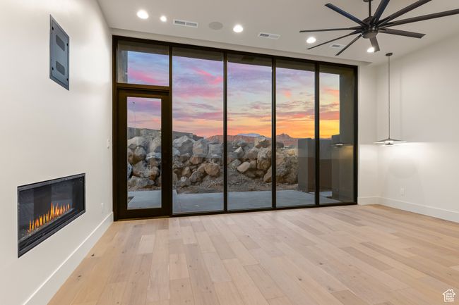 Empty room with ceiling fan, a glass covered fireplace, wood finished floors, and visible vents | Image 35