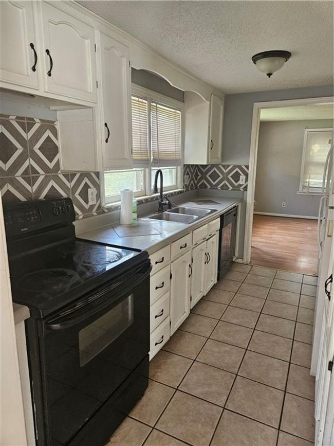 Kitchen featuring range, white cabinetry, light tile patterned floors, dishwashing machine, and a textured ceiling | Image 4