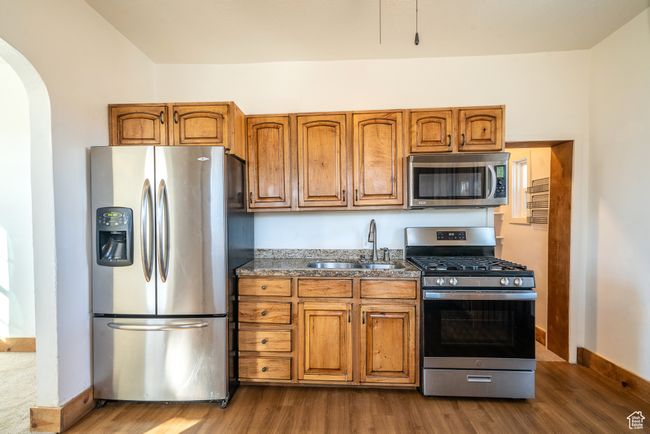 Kitchen featuring stainless steel appliances, arched walkways, brown cabinetry, and a sink | Image 8