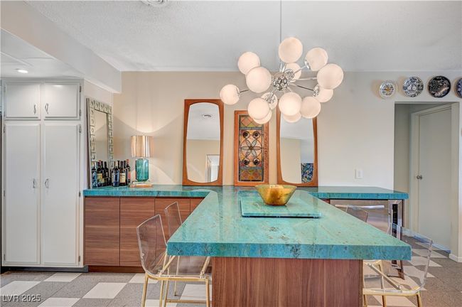 Kitchen featuring a textured ceiling, a notable chandelier, brown cabinets, light floors, and a kitchen bar | Image 14
