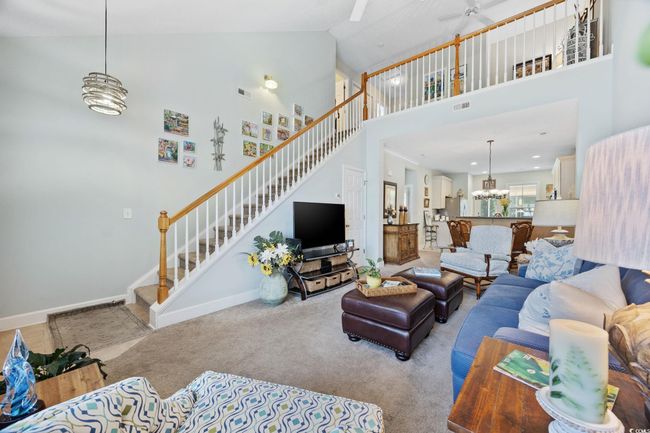 Living room with a chandelier, high vaulted ceiling, stairs, carpet floors, and a ceiling fan | Image 6