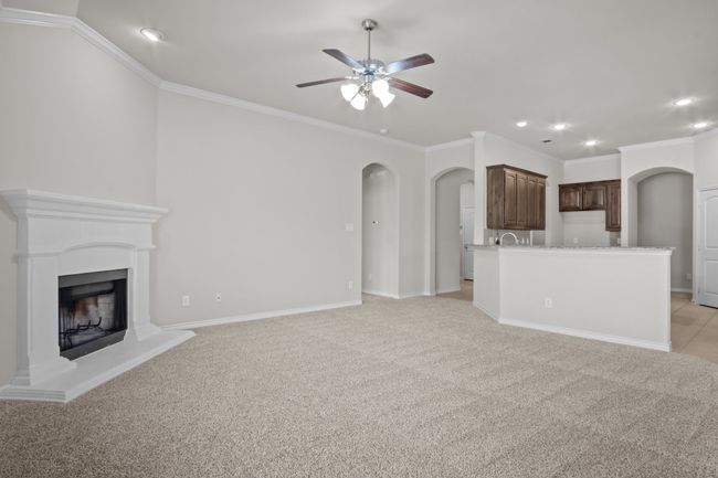 Unfurnished living room featuring ceiling fan, crown molding, arched walkways, a fireplace with raised hearth, and recessed lighting | Image 19