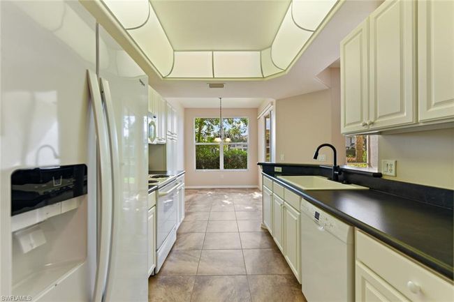 Kitchen with a tray ceiling, a sink, light tile patterned floors, white appliances, and dark countertops | Image 17