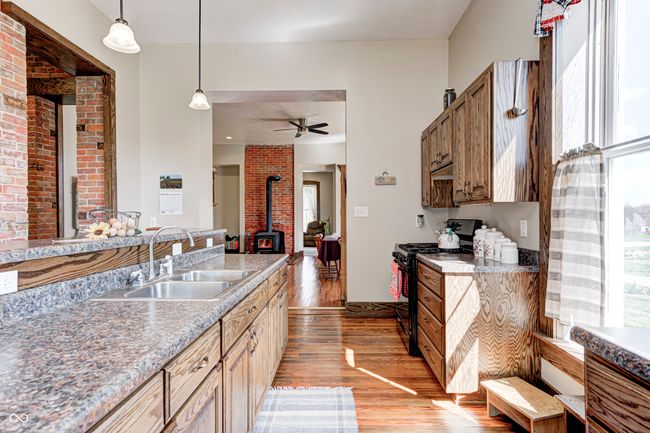kitchen featuring black range with gas stovetop, a wood stove, light wood-style floors, pendant lighting, and a sink | Image 21