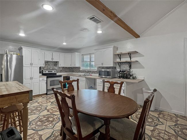 Kitchen featuring stainless steel appliances, decorative backsplash, white cabinetry, open shelves, and light countertops | Image 18