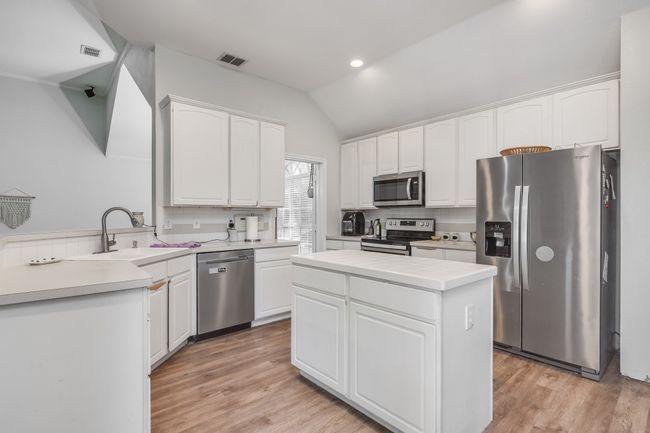 Kitchen featuring stainless steel appliances, a sink, white cabinets, backsplash, and vaulted ceiling | Image 18