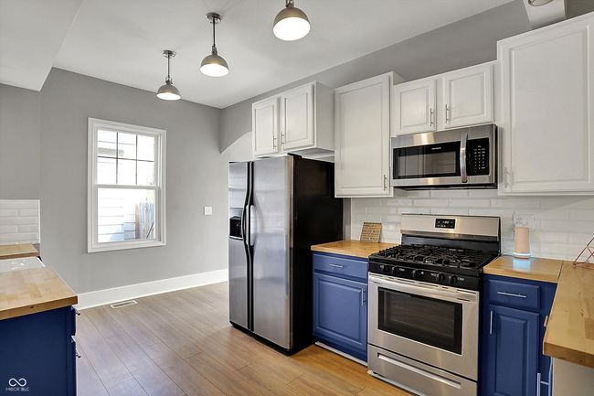 kitchen featuring blue cabinets, butcher block counters, decorative backsplash, and appliances with stainless steel finishes | Image 17