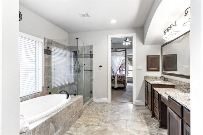 Here’s another view of this luxurious spa-like primary en suite bathroom. With its spacious design, it features elegant finishes that create a serene atmosphere. The bathroom includes dual sinks with a prep vanity, a garden bathtub, a glass-tiled shower with a built-in bench, and a large wardrobe closet. | Image 23