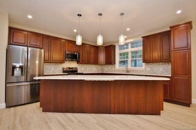 Kitchen with light hardwood / wood-style floors, appliances with stainless steel finishes, hanging light fixtures, and a kitchen island | Image 3