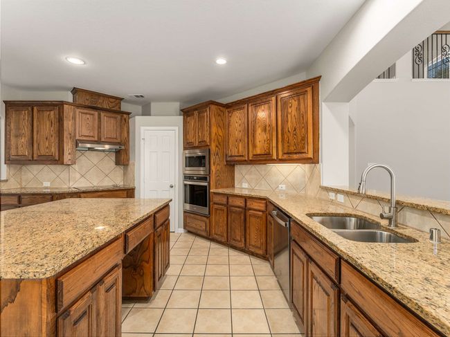 Kitchen with under cabinet range hood, light tile patterned floors, light stone counters, appliances with stainless steel finishes, and a sink | Image 15