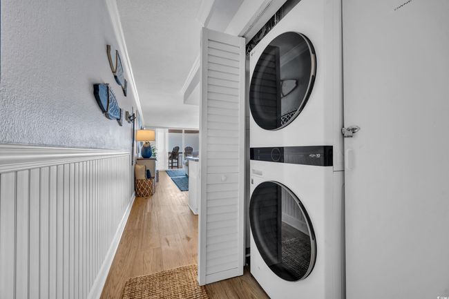 Laundry area featuring estacked washer and dryer and wood finished floors | Image 9