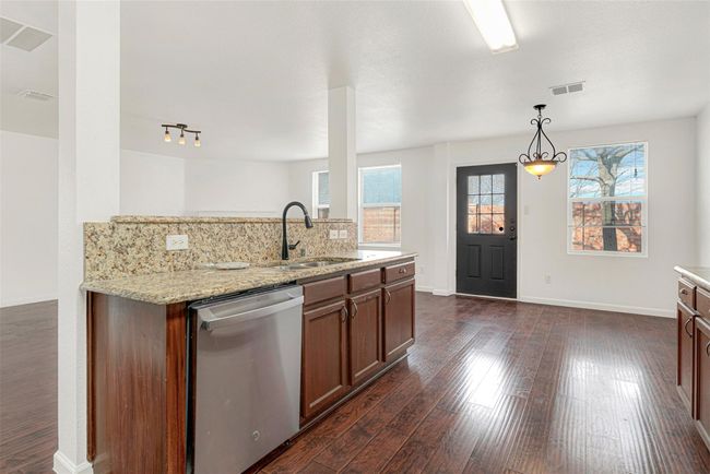 Kitchen featuring stainless steel dishwasher, a sink, dark wood finished floors, and light stone counters | Image 12