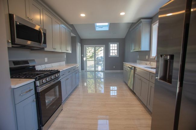 Kitchen with gray cabinetry, vaulted ceiling with skylight, light stone countertops, and stainless steel appliances | Image 7
