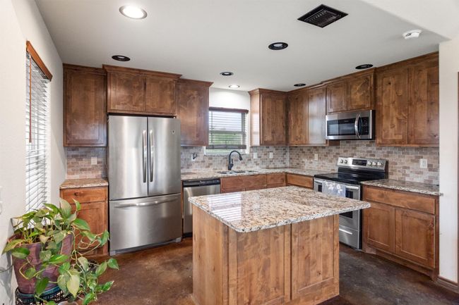 Kitchen featuring a sink, stainless steel appliances, granite countertops, real wood custom cabinets, finished concrete floors, backsplash, and visible vents | Image 4